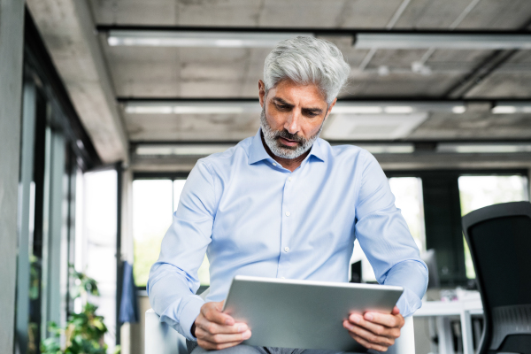 Mature businessman with tablet in the office, reading.