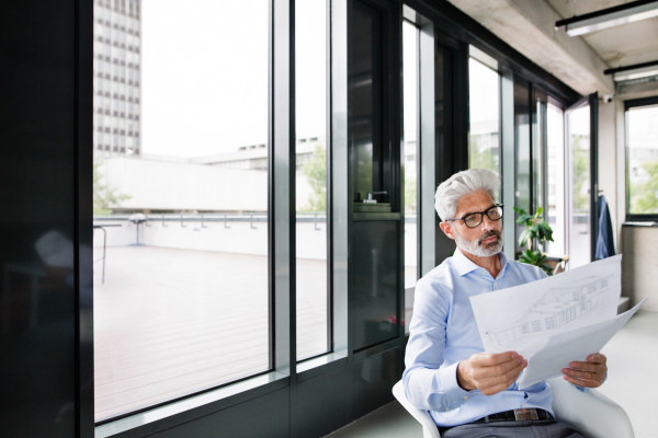 Mature businessman or architect in blue shirt sitting in the office, reading plans.