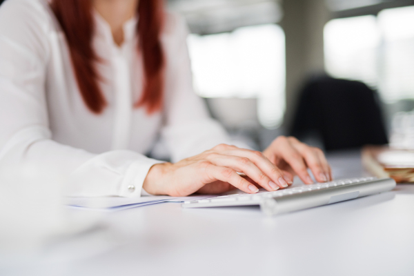 Unrecognizable young businesswoman in her office, sitting at the desk, working on laptop.