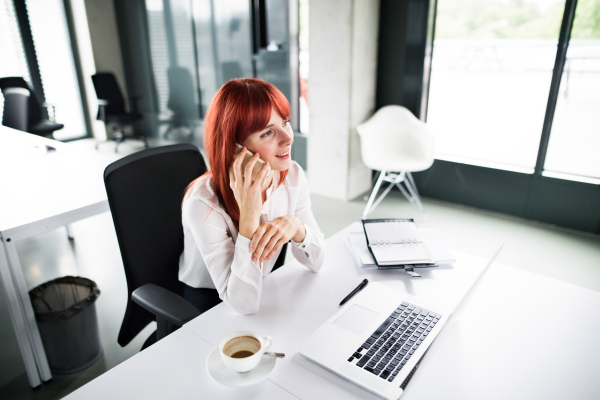 Businesswoman with laptop and smart phone making a phone call in her office.