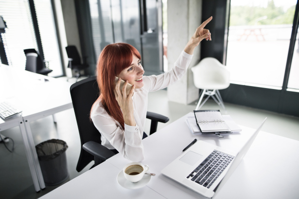 Businesswoman with laptop and smart phone making a phone call in her office.