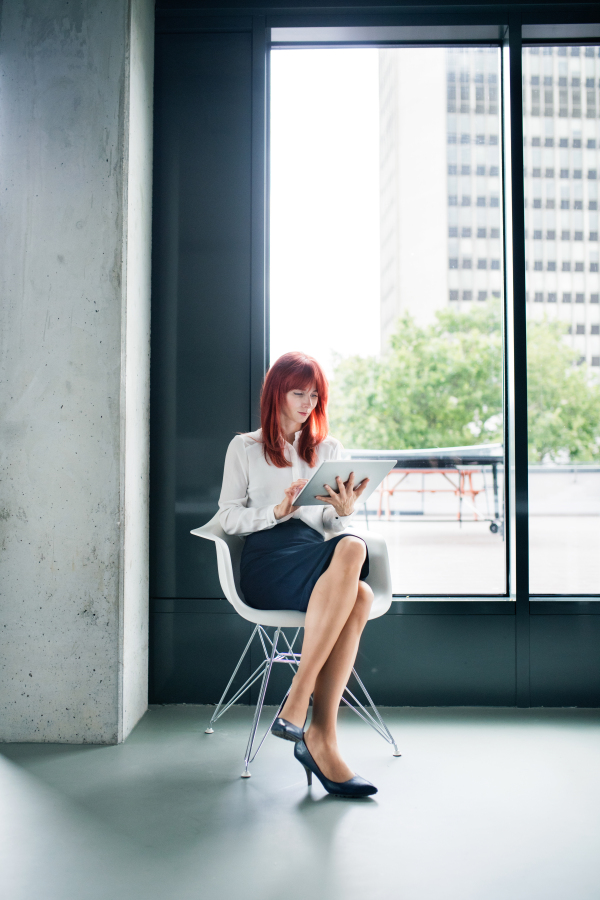 Beautiful young businesswoman with tablet in her office sitting on chair, working.