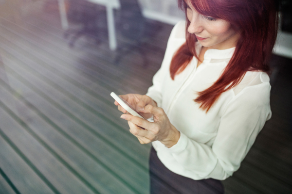 Beautiful young businesswoman with smartphone in her office working.