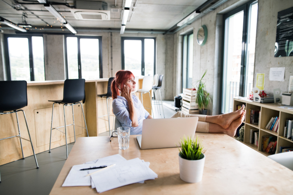 Beautiful businesswoman in the office, with her feet up on desk, making a phone call.