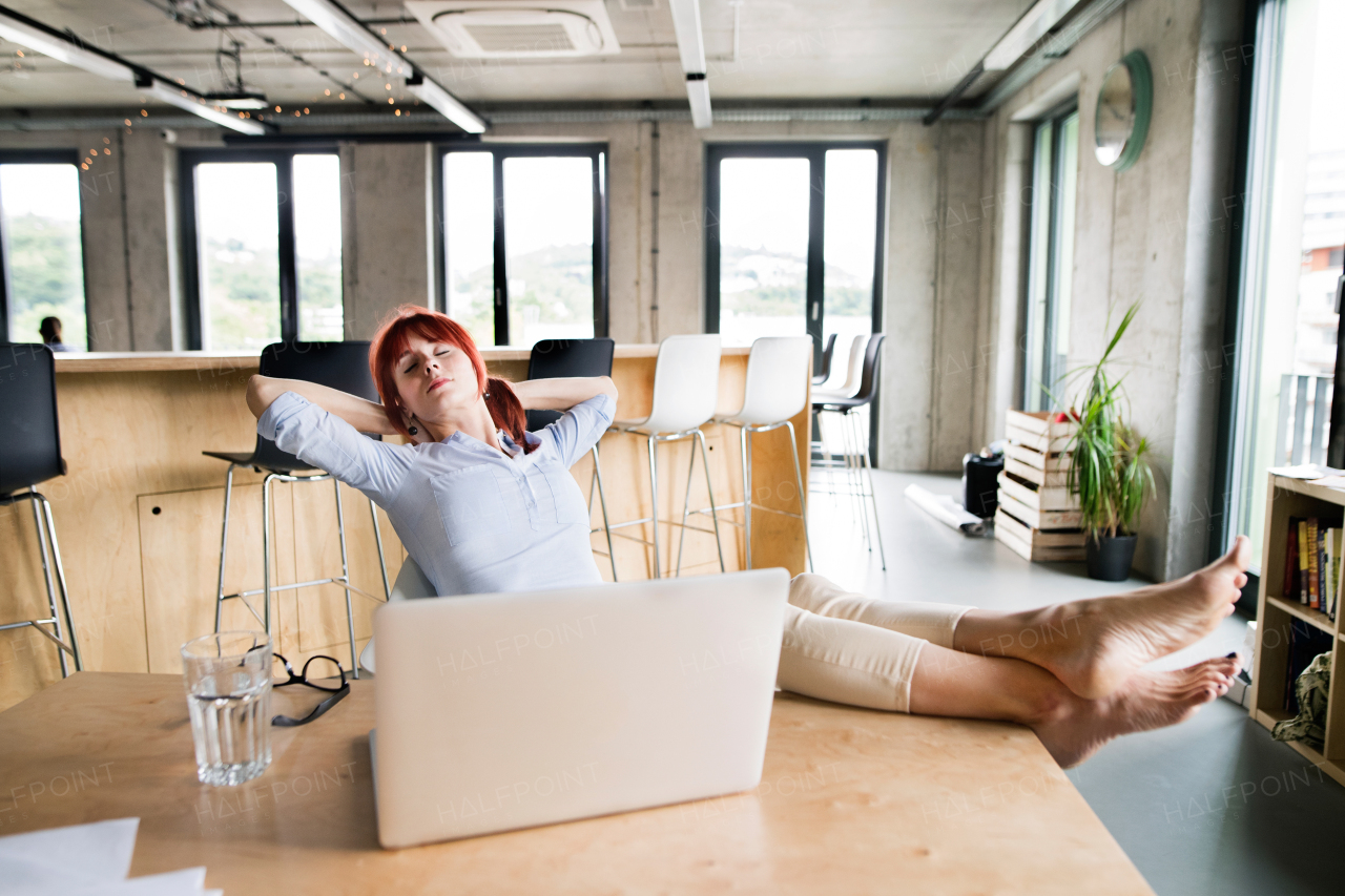 Beautiful businesswoman with laptop in the office with her feet up on desk.