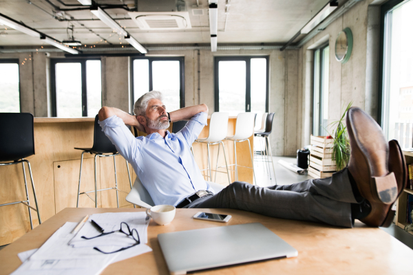 Thoughtful mature businessman with gray hair in the office with feet up on desk.