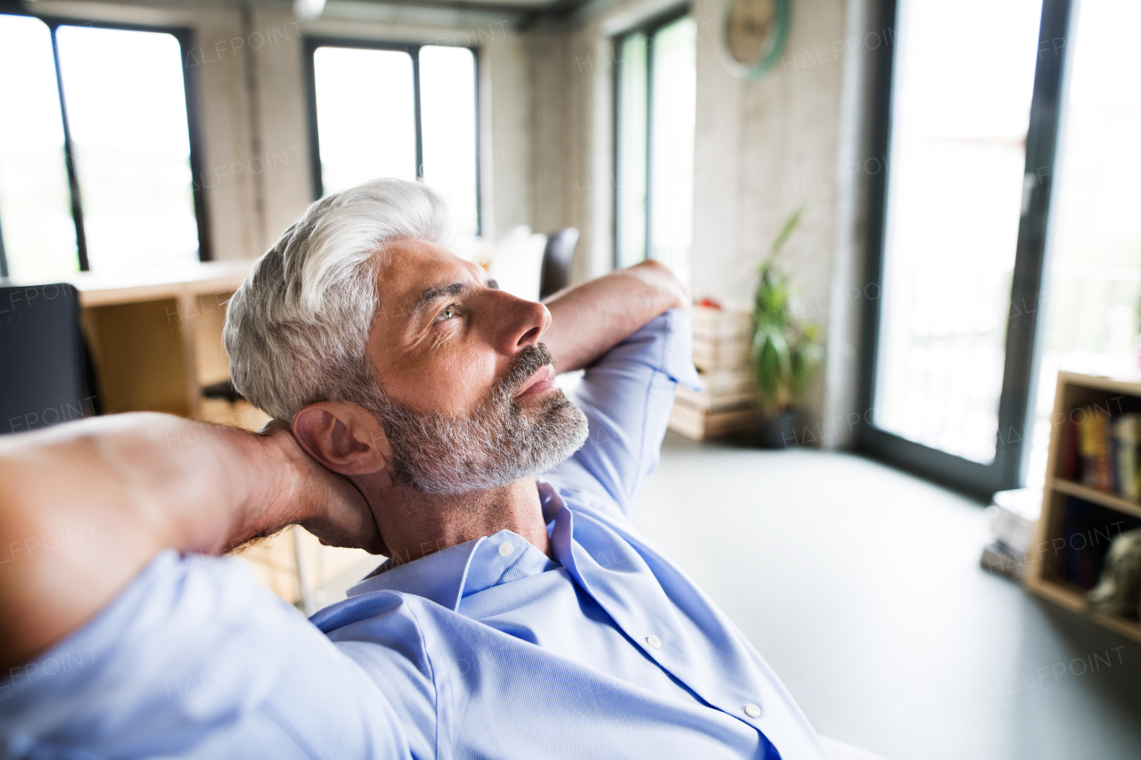 Thoughtful mature businessman with gray hair in the office wearing a blue shirt.