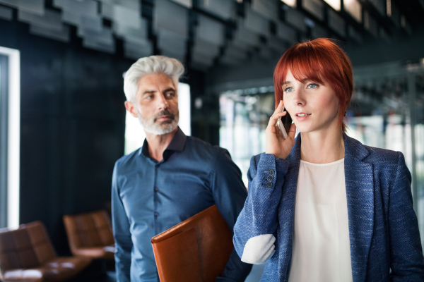 Two business people in the workplace. Businesswoman with smart phone making a phone call.