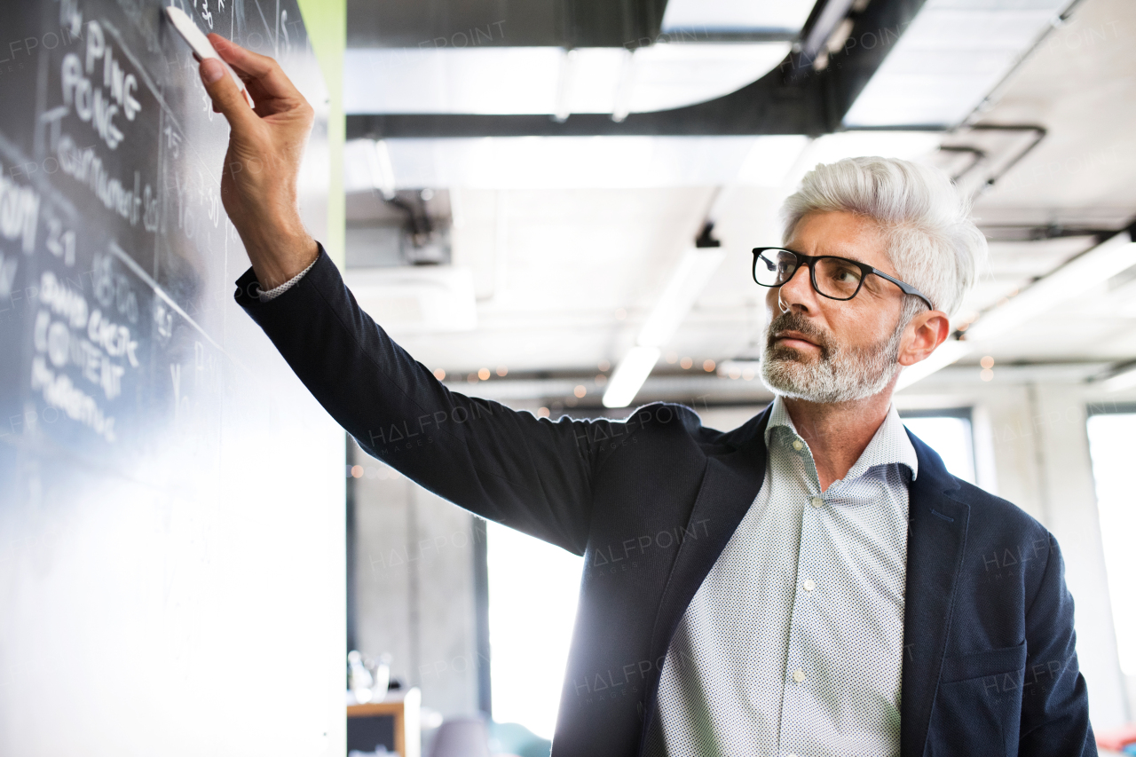 Handsome mature businessman with gray hair in the office writing notes on blackboard, setting goals.