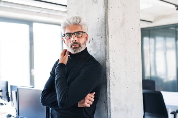 Handsome mature businessman with gray hair in black turtleneck and eyeglasses in the office.