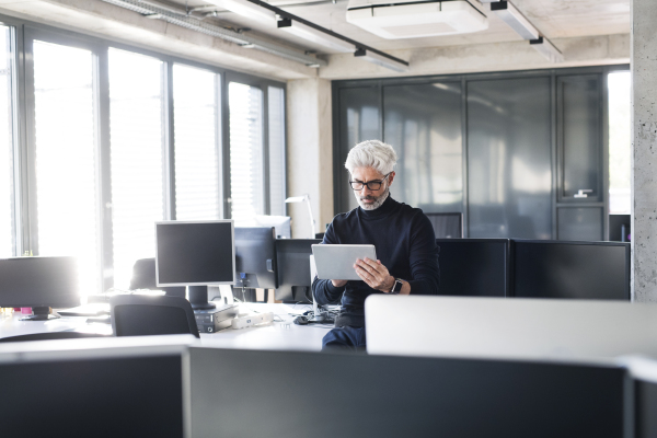 Handsome mature businessman with tablet in the office working, reading documents.