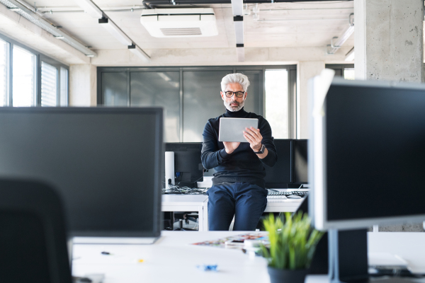 Handsome mature businessman with tablet in the office working, reading or searching something.