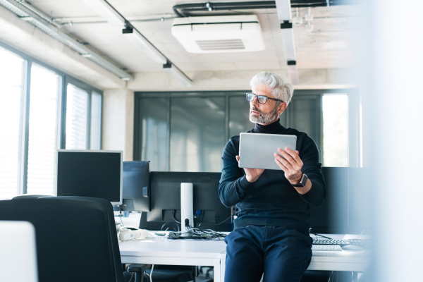 Handsome mature businessman with tablet in the office working, reading or searching something.