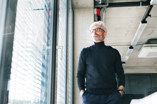 Handsome mature businessman with gray hair in black turtleneck and eyeglasses in the office.