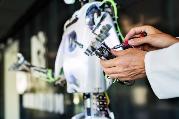 Unrecognizable scientist with a robot, mending or inventing.