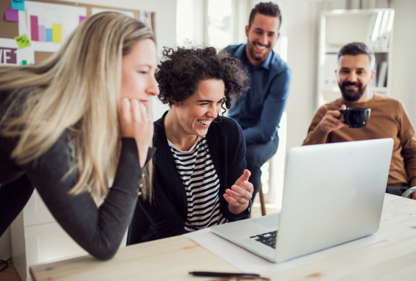 Group of young cheerful male and female businesspeople with laptop working together in a modern office.