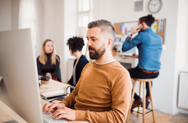 Group of young concentrated male and female businesspeople with computer and smartphone working in a modern office.