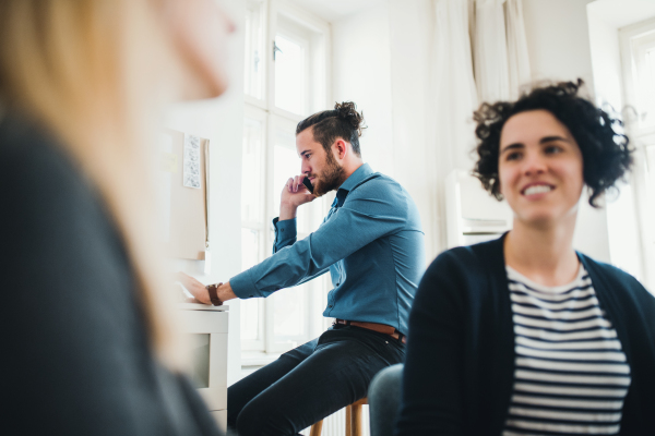 Group of young, cheerful, male and female businesspeople with smartphone working together in a modern office.