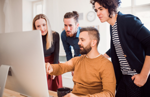 Group of young,cheerful, male and female businesspeople looking at laptop screen in a modern office, discussing issues.