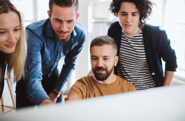 Group of young,cheerful, male and female businesspeople looking at laptop screen in a modern office, discussing issues.