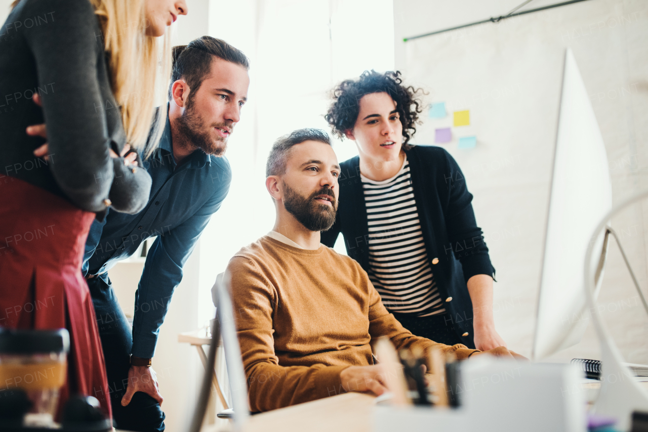 Group of young concentrated male and female businesspeople with computer working together in a modern office.