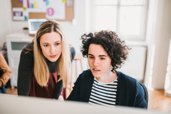 Two female business people with desktop computer in a modern office, working.