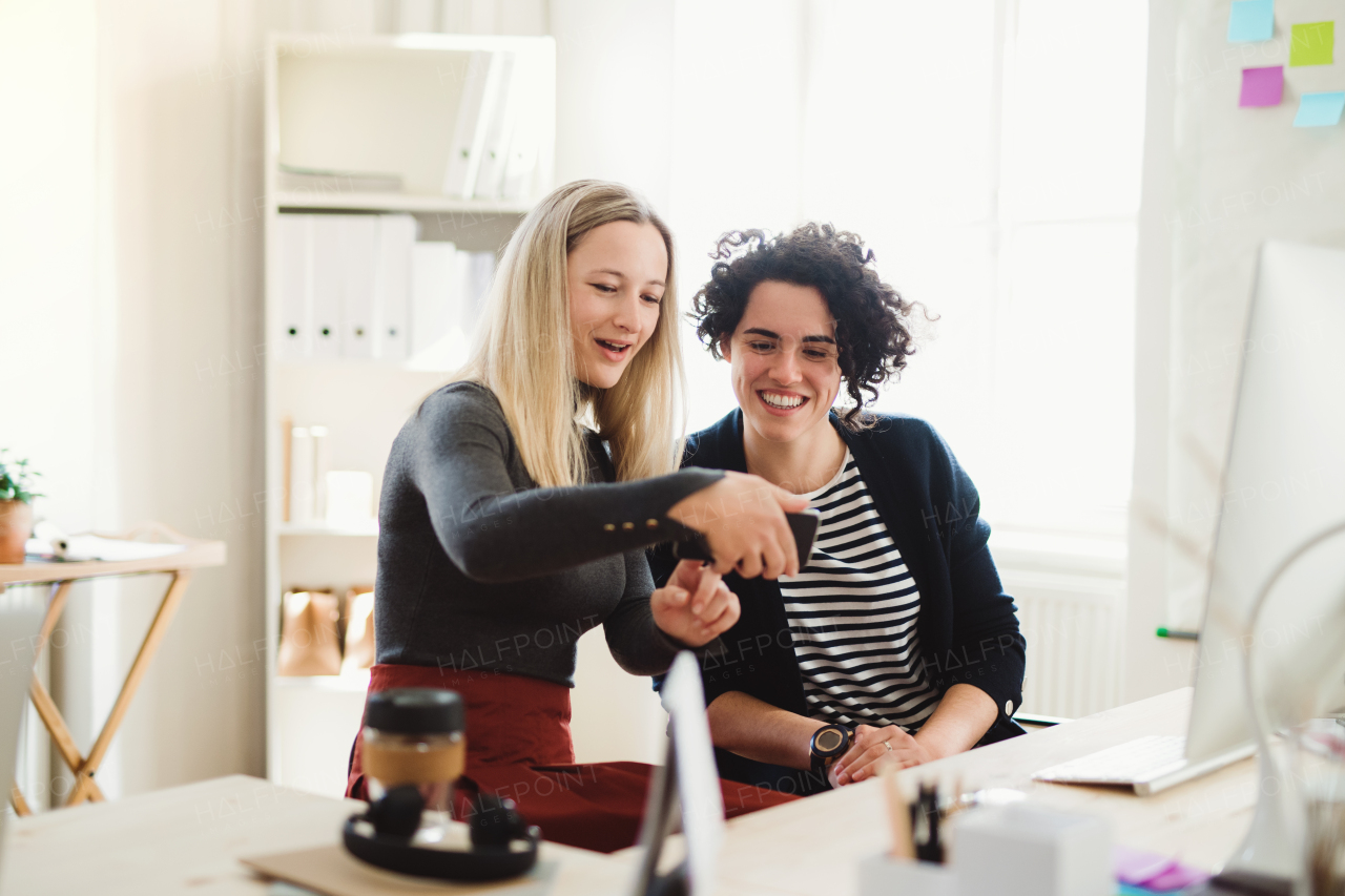 Group of young happy female businesspeople with smartphone talking in a modern office.