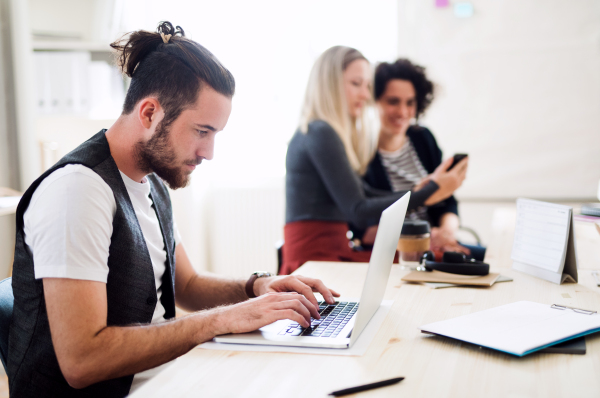 Group of young concentrated male and female businesspeople with laptop and smartphone working in a modern office.