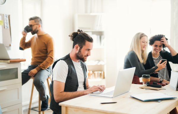 Group of young concentrated male and female businesspeople with laptop and smartphone working in a modern office.