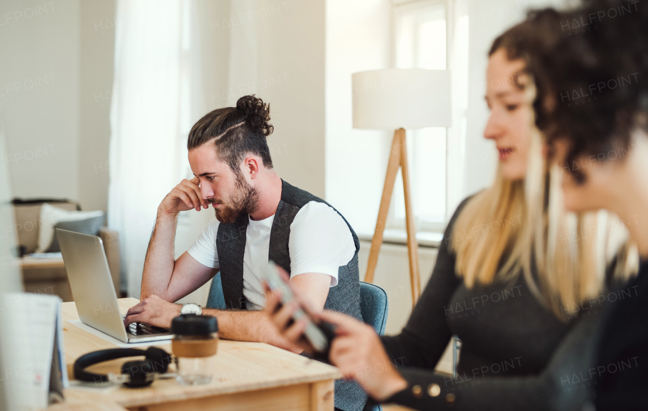 Group of young, cheerful, male and female businesspeople with smartphone and laptop working together in a modern office.