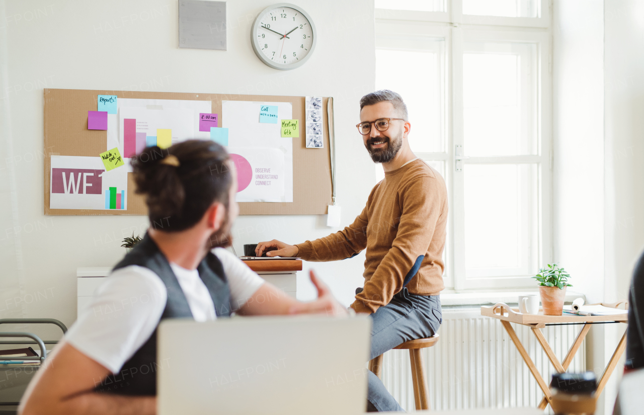 Two young hipster male businesspeople with laptop talking in a modern office.