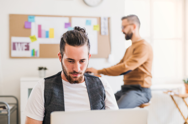 Two young hipster male businesspeople with computer working in a modern office.