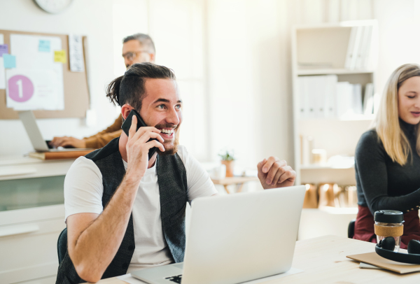 Group of young, cheerful, male and female businesspeople with laptop and smartphone working together in a modern office.