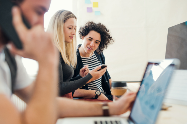 Group of young concentrated male and female businesspeople with laptop and smartphone working together in a modern office.