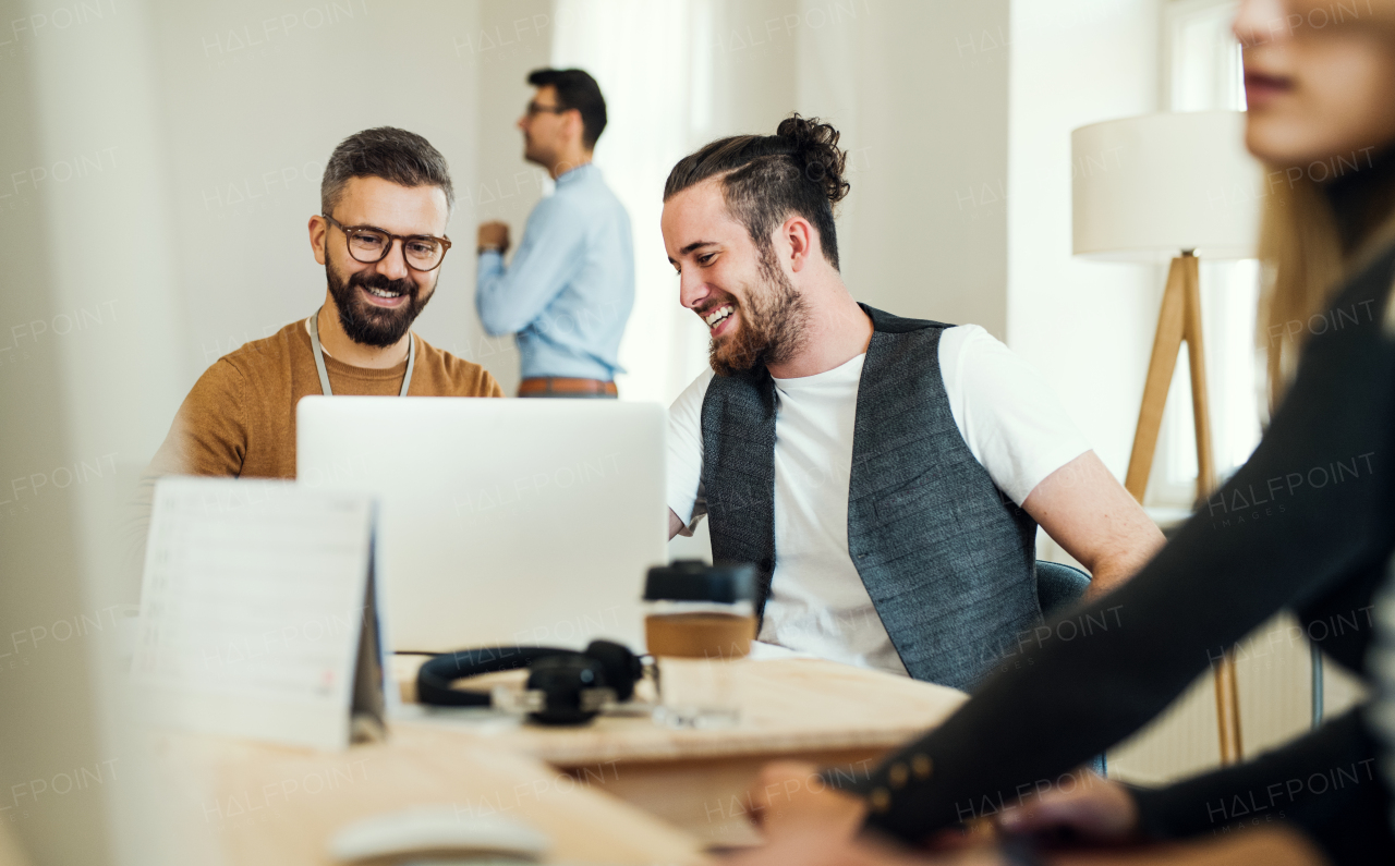 Group of young concentrated male and female businesspeople with laptop working together in a modern office.