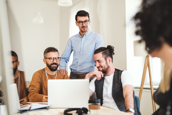 Group of young, cheerful businesspeople sitting around table in a modern office, having meeting.