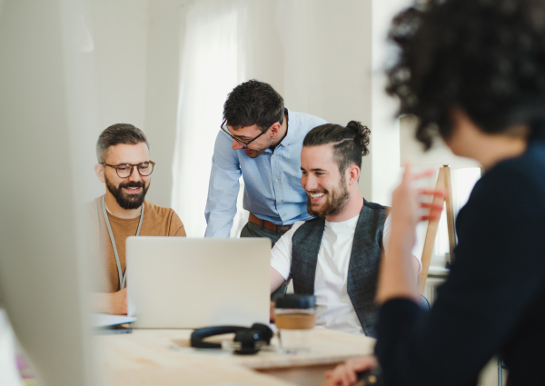 Group of young, cheerful, male and female businesspeople with laptop working together in a modern office.