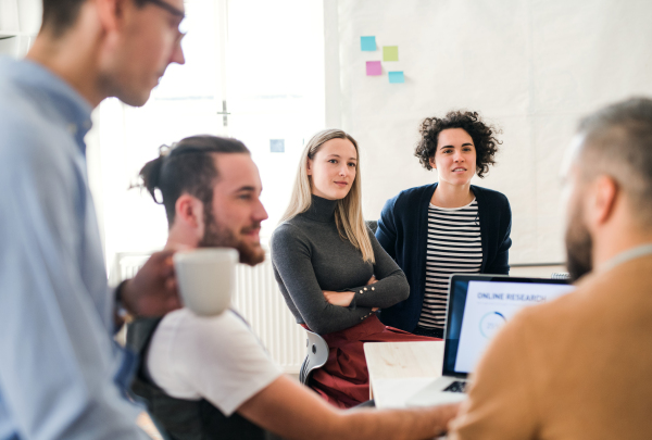 Group of young, cheerful, male and female businesspeople with laptop working together in a modern office.