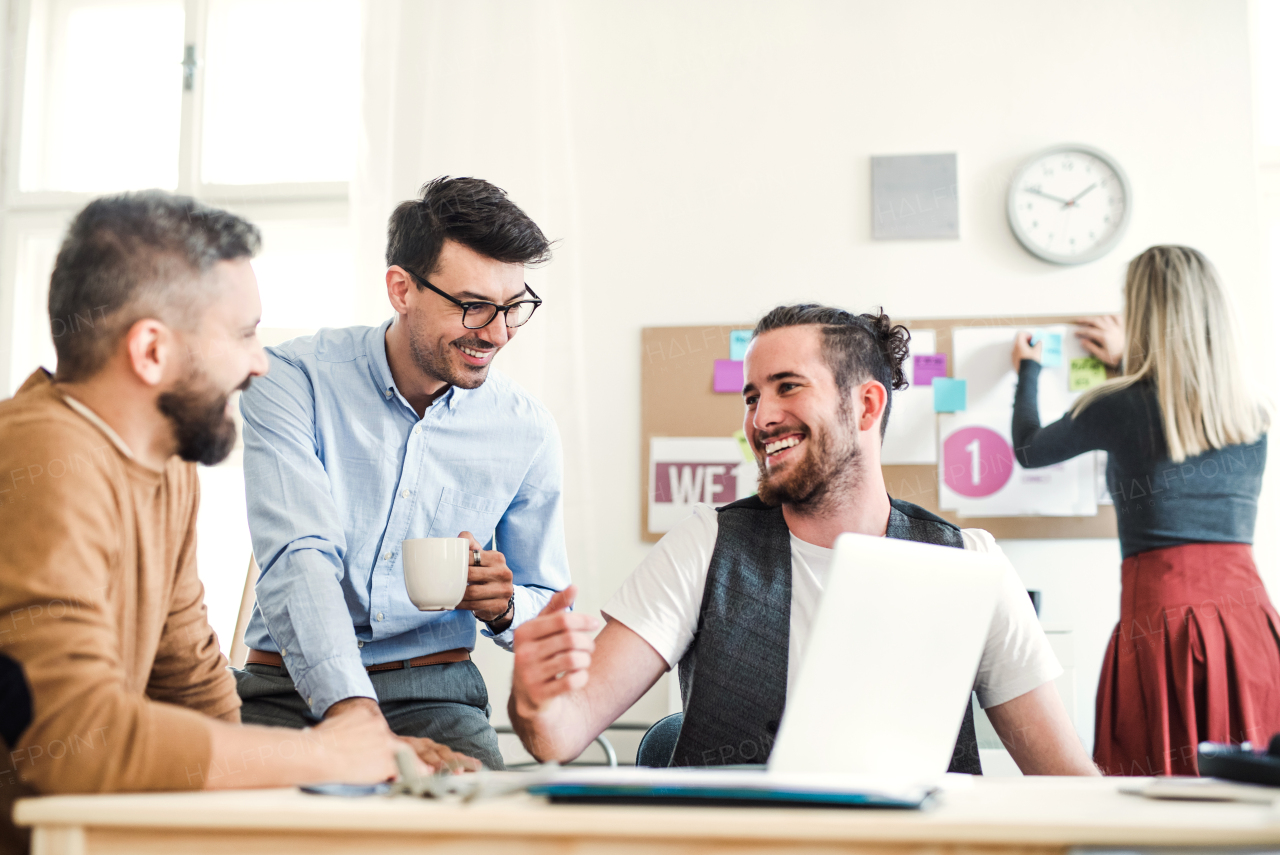 Group of young, cheerful, male and female businesspeople with laptop working together in a modern office.