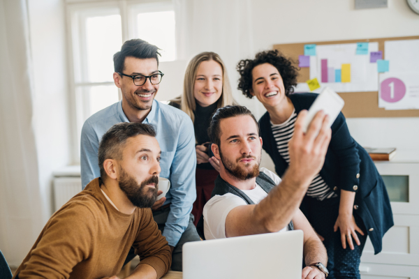 Group of young,cheerful, male and female businesspeople with smartphone in a modern office, taking selfie.