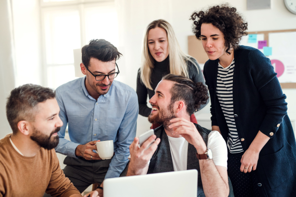 Group of young, cheerful, male and female businesspeople with laptop working together in a modern office.