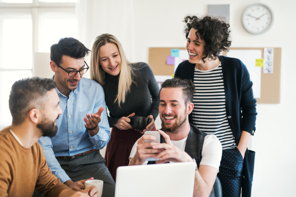 Group of young cheerful male and female businesspeople with laptop and smartphone having meeting in a modern office.