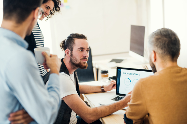 Group of young concentrated male and female businesspeople with laptop working together in a modern office.