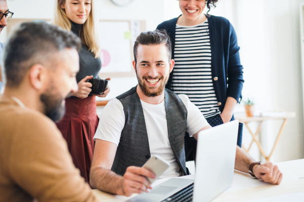 Group of young, cheerful, male and female businesspeople with laptop working together in a modern office.