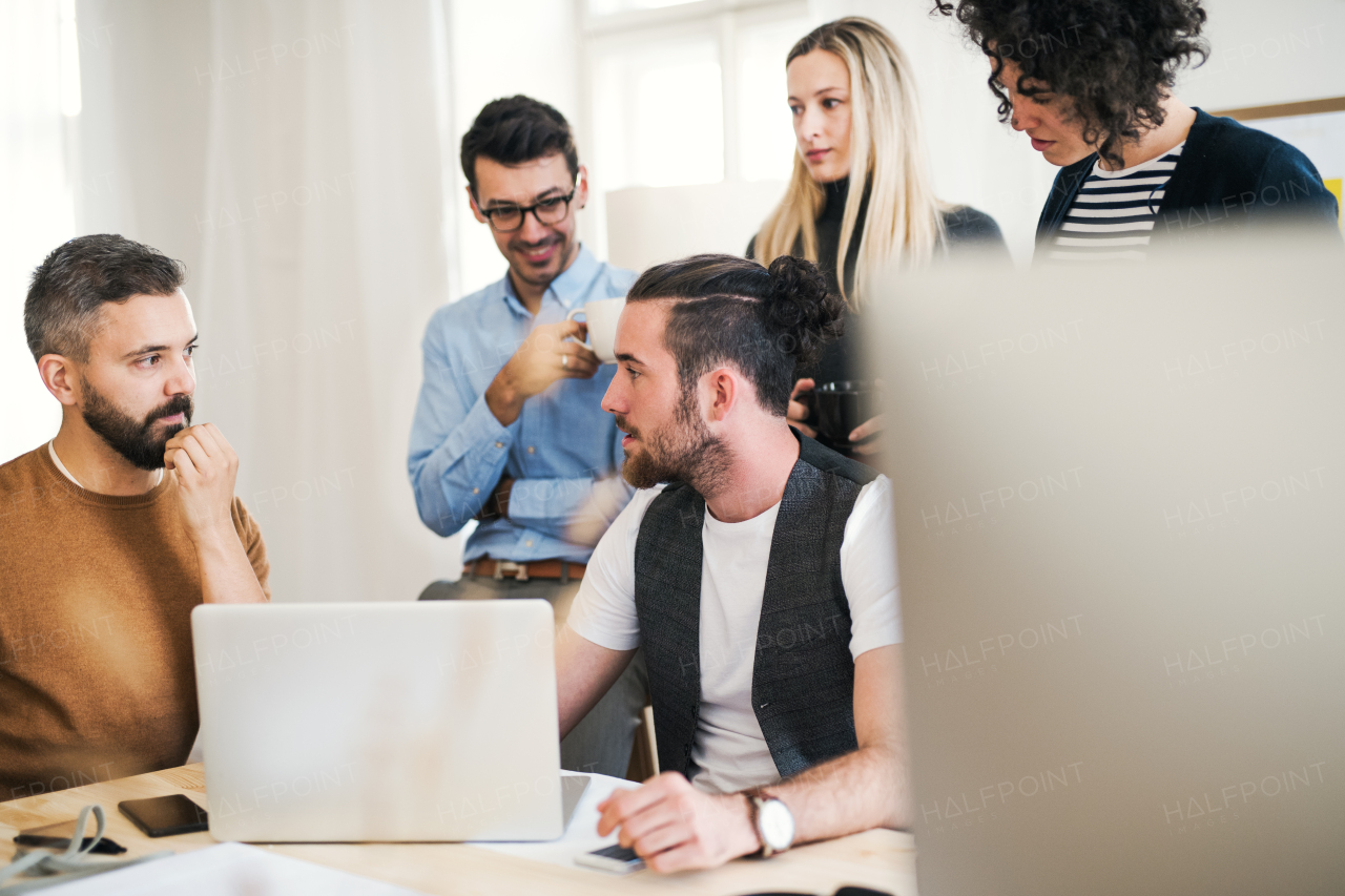 Group of young concentrated male and female businesspeople with laptop having meeting in a modern office.