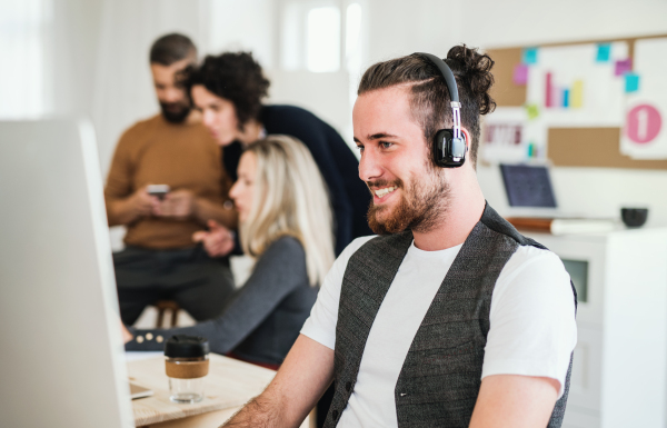 A portrait of young hipster businessman with headphones and colleagues in a modern office, laughing.