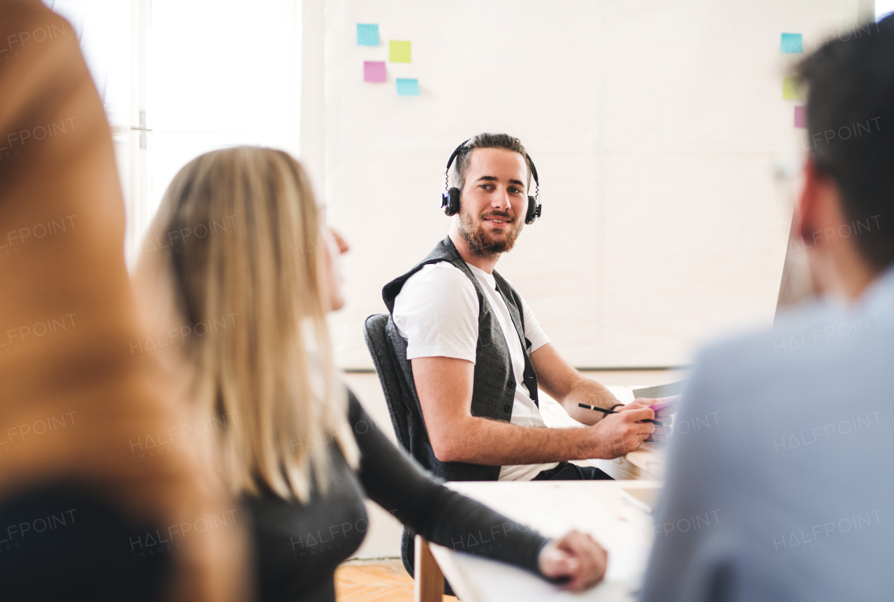 A portrait of young hipster businessman with headphones and colleagues in a modern office.