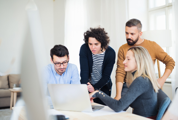 Group of young, cheerful, male and female businesspeople with laptop working together in a modern office.