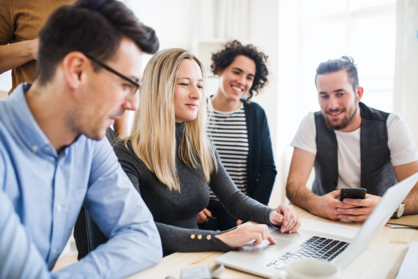 Group of young, cheerful, male and female businesspeople with laptop working together in a modern office.