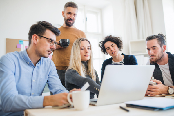 Group of young, cheerful, male and female businesspeople with laptop working together in a modern office.